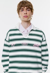 Zielono-biały w paski longsleeve polo. Posiada kołnierzyk, różowe hafty i logotypy. Miękka tkanina o luźnym kroju.