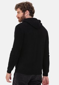 Schwarze Kapuzenjacke mit strukturierten Fleeceärmeln und glattem Körper. Verfügt über gerippte Bündchen und Saum, konzipiert für Wärme und Komfort.