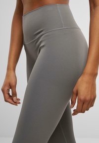 Leggings grişo înalte dintr-un material elastic neted, având un design cu cusături plate și o siluetă ajustată, cu un aspect curat și minimalist.