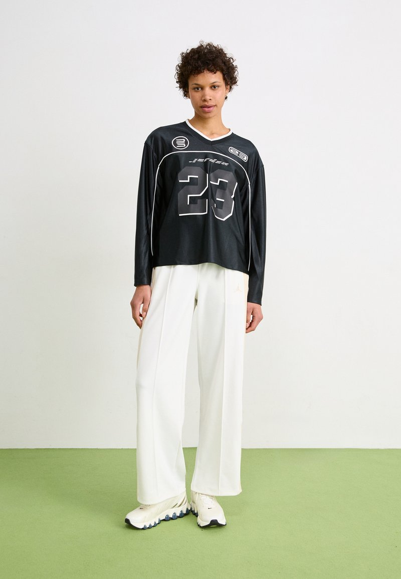 Schwarzes Langarmshirt mit der Aufschrift "23" in Grau, kombiniert mit weißen weitem Hosen und weißen Sneakers. Einfaches Design mit lockerer Passform.