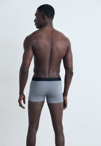 Szürke boxer alsónadrág fekete derékbőséggel, testes kialakítással és sima textúrával, hátulról nézve egy modellen, világos háttér előtt.
