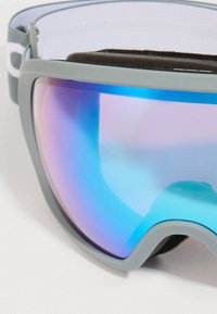 Síszemüveg szürke kerettel, kék-lila tükröző lencsével, fekete habszivaccsal és szürke állítható pánttal, amelyen fehér logó található.