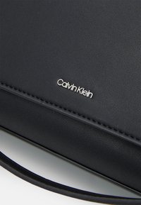 Borsa a tracolla in ecopelle nera di Calvin Klein con una superficie liscia, cuciture sottili e un accento in logo metallico.