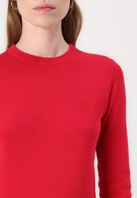 Maglione rosso a maglia con scollo a girocollo a costine e maniche lunghe. Presenta il logo "HUGO" ricamato dello stesso colore sul petto.