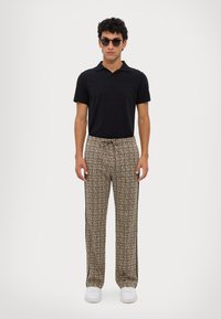 Musta polo-paita yhdistettynä kuvioituihin, joustavaan vyötäröön omaaviin housuihin, joissa on moniväriset ruudut ja mustat sivuraitat; malli käyttää aurinkolaseja.