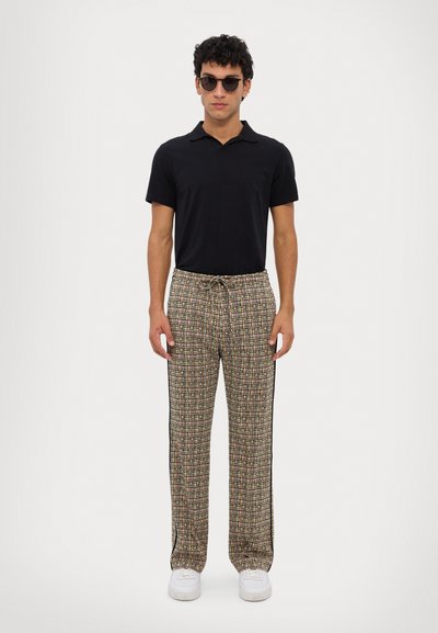 Black polo shirt paired with patterned, elastic-waist pants featuring multicolored checks and black side stripes; model wears sunglasses.