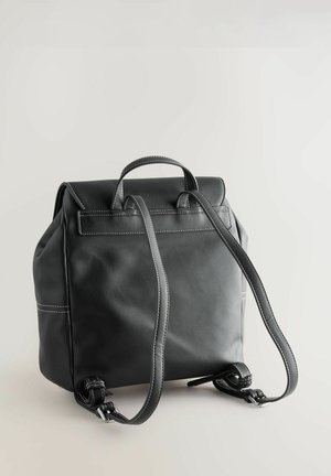Fekete bőrből készült hátizsák strukturált kialakítással, kontrasztos fehér varrással, felső fogantyúval és állítható pántokkal. Simább textúra és minimalista stílus.
