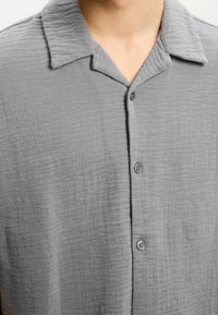 Graues Hemd mit Kragen aus strukturiertem Stoff, fünf Knöpfen und einem lockeren Schnitt. Der Kragen ist weich und leger gestaltet.