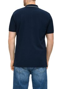 Granatowa koszulka polo z kontrastowym białym kołnierzykiem i wykończeniami rękawów, wykonana z bawełny, w zestawie z jasnoniebieskimi szortami dżinsowymi.