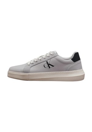 Sneaker bianco basso con chiusura frontale con lacci, logo nero sul lato e suola beige, con toppa nera sul tallone per contrasto.