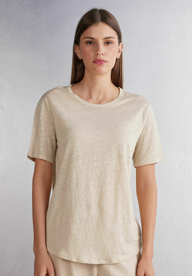 Béžové tričko s krátkým rukávem vyrobené z lehkého, texturovaného materiálu s kulatým výstřihem a mírně zakřiveným lemem.