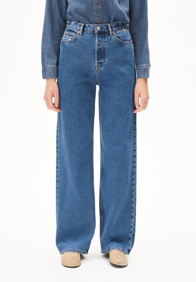 Högmidjade vida jeans i medelblå denim. Funktioner inkluderar fem fickor, metalldetaljer och fransad fåll.