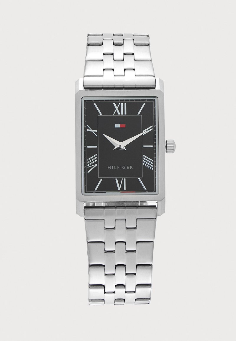 Montre-bracelet en métal argenté avec cadran noir rectangulaire, chiffres romains blancs, deux aiguilles argentées et logo Hilfiger sous 12 heures.