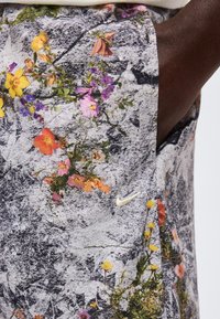 Κοντινή λήψη σορτσάκι με floral μοτίβο με πορτοκαλί, κίτρινα και μοβ λουλούδια σε υφασμένο γκρι φόντο, με μικρό λευκό λογότυπο Nike.