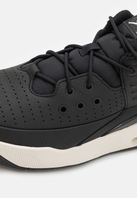 Close-up af sort sneaker med perforeret læderoverdel, sorte snørebånd, polstret tunge og hvid gummisål.