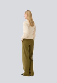 Cremfarbener Strickpullover und grüne weite Hose, von hinten betrachtet. Der Pullover hat eine strukturierte Gestaltung; die Hose verfügt über seitliche Taschen.