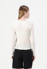 Lett, kremfarget langermet topp med en jevn tekstur, med en buet yoke-detalj og en slim fit. Kombinert med svarte shorts.