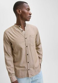 Light brown long-sleeve shirt with a mandarin collar, front pocket, and dark buttons. Smooth fabric with a subtle texture.