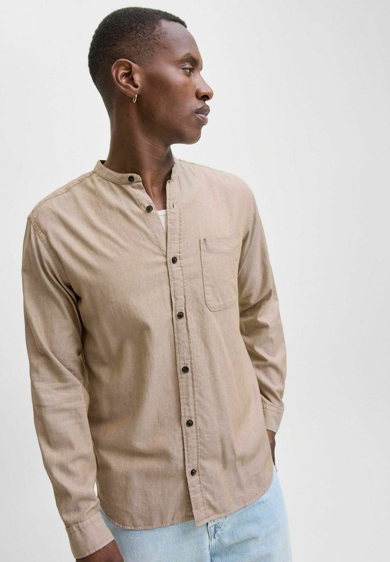 Light brown long-sleeve shirt with a mandarin collar, front pocket, and dark buttons. Smooth fabric with a subtle texture.
