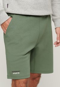 I pantaloni corti in cotone verde combinato presentano tasche laterali, un design semplice e un piccolo logo sull'orlo sinistro, offrendo un look atletico casual.