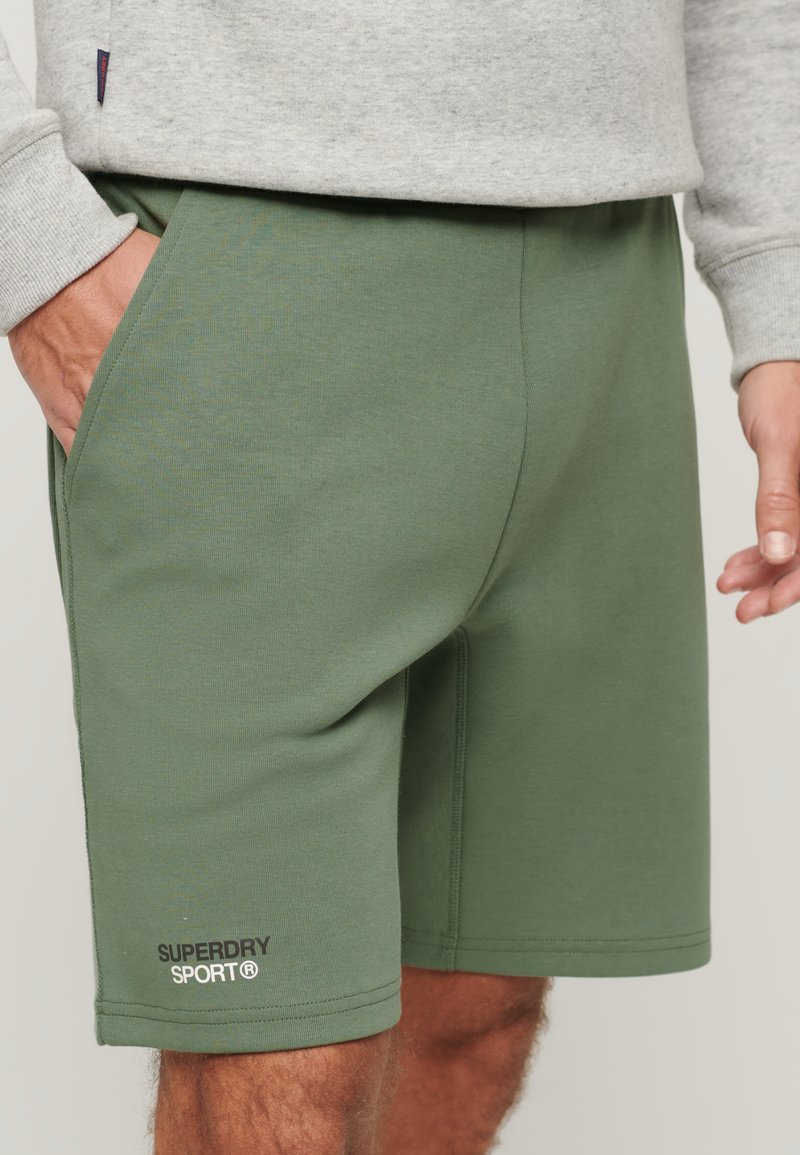 I pantaloni corti in cotone verde combinato presentano tasche laterali, un design semplice e un piccolo logo sull'orlo sinistro, offrendo un look atletico casual.
