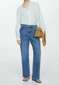 Blouse à rayures bleu clair avec manches longues, devant boutonné, associée à un jean en denim bleu taille haute et un accessoire pull marron clair.