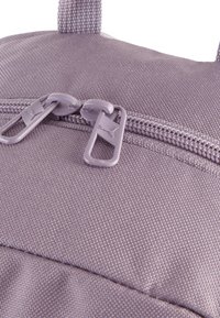 Mochila de tela de color púrpura claro con una superficie texturada, que cuenta con dos cremalleras y una asa en la parte superior para un fácil transporte.