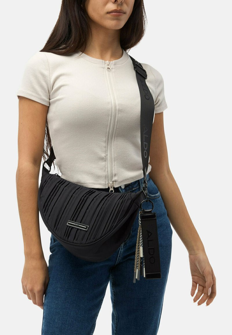 Černá ramenní taška s plisé texturou, stříbrnými detaily a nastavitelným popruhem. Nositá přes rameno k casual outfitu.