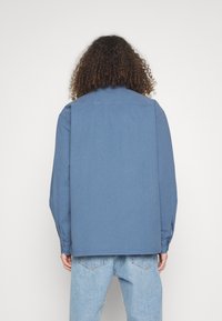 Blauwe denimoverhemd met lange mouwen, knoopsluiting en een klassieke kraag. Ontspannen pasvorm, met een gladde textuur en geen zichtbare patronen.