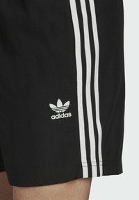 Czarne spodenki sportowe z trzema białymi paskami po bokach i białym logo Adidas na lewej nogawce. Lekki materiał, gładka tekstura.