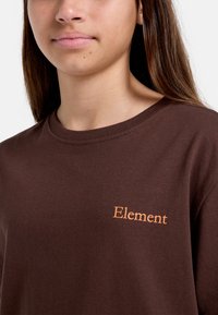 Brun bomull t-shirt med rund halsringning och korta ärmar. Fram kan man se "Element" i orange bokstäver. Mjuk textur.