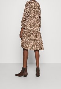 Kleid mit Leopardenmuster, langen Ärmeln, gestuftem Design und lockerer Passform. Kombiniert mit braunen Ankle Boots mit strukturiertem Muster.