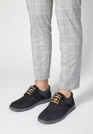 Marineblauwe casual schoenen met een gestructureerde afwerking, voorzien van bruine veters, contrasterende stiksels en grijze rubberen zolen, gecombineerd met geruite broek.