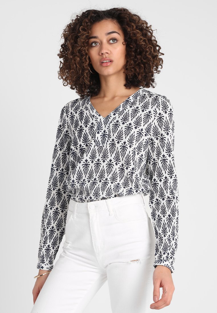 Langærmet skjorte i hvid og marineblå med blomsterprint, V-udskæring og rynkede manchetter, kombineret med hvid slidte jeans.