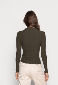 Haut vert foncé à manches longues côtelé avec un ourlet festonné et une coupe ajustée. Le tissu a une finition texturée, mettant en valeur la silhouette.