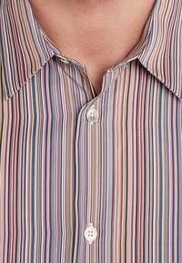 Mand iført en multicolor vertikalt stribet skjorte med knapper, kraven åben og viser huden på halsen.