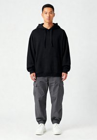 Fekete, oversize kapucnis pulóver kenguru zsebbel és húzózsinórral, szürke cargo nadrággal párosítva, oldalzsebekkel és elasztikus mandzsettával. Fehér sportcipők.