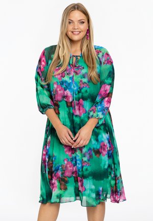 Blumenkleid aus grünem Stoff mit rosa und blauen Akzenten. Hat einen lockeren Schnitt, lange Ärmel und ein gebundenes Halsdetail. Leicht und fließendes Design.