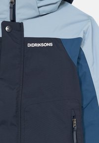 Didriksons plava i tamnoplava jakna s patentnim zatvaračem i kapuljačom, logotipom na prsima, gumbom na kopčanje i džepom s patentnim zatvaračem sprijeda.
