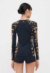 Long-sleeve swim top in navy with gold and pink abstract patterns; fitted design with slim sleeves and ribbed texture. Paired with black shorts.