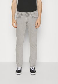 Grå denimjeans med smal passform. Har beltesløyfer, frontlommer og en falmet tekstur. Kombinert med svarte sneakers og en svart skjorte.