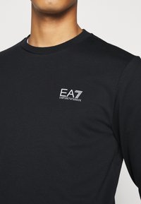 Felpa nera in cotone, con scollo tondo e logo EA7 Emporio Armani bianco sul lato sinistro del petto.