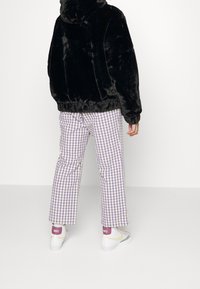 Sort faux fur hættetrøje, ternede lilla og hvide bukser og hvide sneakers med pink accenter. Outfittet har en afslappet pasform.