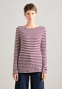 Langermet stripete skjorte med burgunder- og hvite horisontale striper, med bred båthals og myk stoff. Kombinert med mørkeblå bukser.