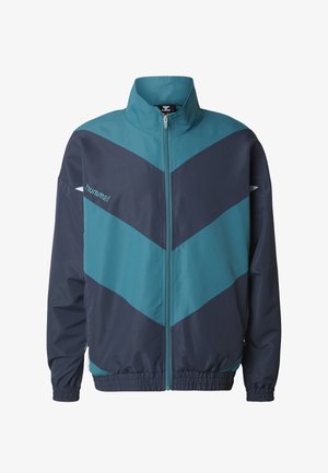Løpejakke i blågrønn og marineblå med høy krage, full glidelås og chevronmønster. Laget av glatt stoff med elastiske mansjetter og kant.