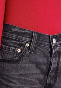 Černé džíny z denimu s texturovaným povrchem, pěti kapsami a oranžovým šitím na kovových prvcích, spárovány s červeným přiléhavým topem.