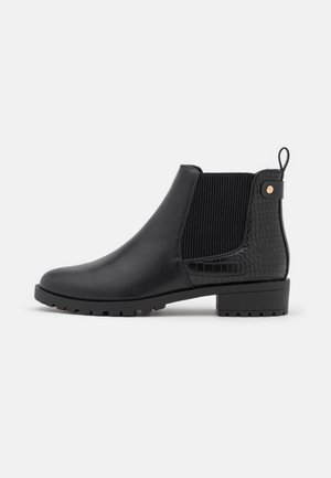 Bottine en cuir noir avec panneaux élastiques sur les côtés, talon texturé, languette de tirage et petit talon bloc, sur fond blanc.