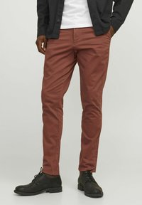 Czerwone chinosy w kolorze rdzy o slim fit, wykonane z bawełnianej tkaniny. Charakteryzują się kieszeniami z przodu i z tyłu, w połączeniu z czarnymi butami na sznurówki.