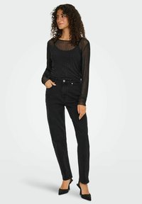 Sort, gennemsigtig langærmet top med prikket tekstur, parret med højtaljede sorte jeans og spidse hæle. Simpel, tætsiddende design.
