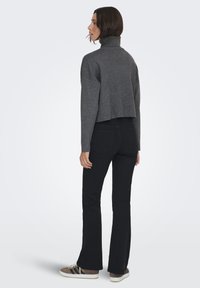 Maglione grigio corto con colletto alto, abbinato a jeans neri a zampa d'elefante. L'outfit presenta un tessuto testurizzato, e le scarpe sono marroni e bianche.